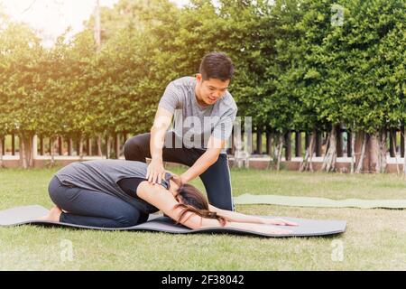 Asiatische Mann und Frau Training Yoga im Freien in meditieren Pose sitzen auf grünem Gras. Junges Paar üben Stretching tun in der Natur einen Feldgarten Stockfoto