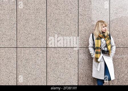 Eine blonde Frau mit einer Retro-Kamera steht gegen die Wand und schaut weg. Freiraum. Kopierraum Stockfoto