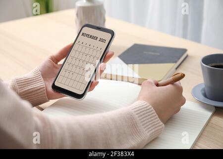 Frau mit Handy mit Kalender-Anwendung am Tisch Stockfoto