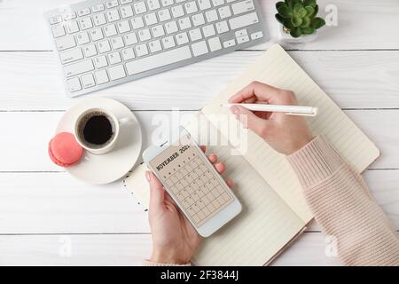 Frau mit Handy mit Kalender-Anwendung am Tisch Stockfoto