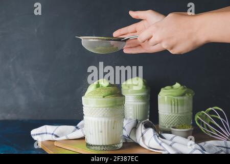 Frau bereitet leckere dalgona Matcha Latte auf dunklem Hintergrund Stockfoto