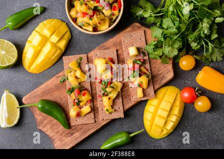 Komposition mit frischer Mango-Salsa und Knäckebrot auf dunklem Grund Stockfoto