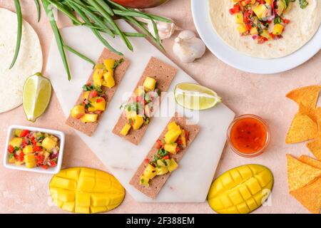 Komposition mit frischer Mango-Salsa, Knäckebrot und Nachos auf farbigem Hintergrund Stockfoto