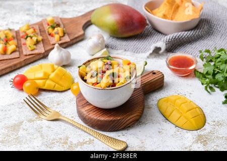 Komposition mit frischer Mango-Salsa, Knäckebrot und Nachos auf hellem Hintergrund Stockfoto