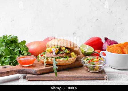 Komposition mit Burger, frischer Mango-Salsa und Nachos auf dem Tisch Stockfoto