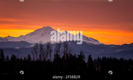 Roter, oranger und gelber Himmel bei Sonnenaufgang über Mount Baker, einem schlafenden Vulkan im Staat Washington, USA. Blick vom Fraser Valley von British Columbia Stockfoto