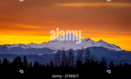 Roter, oranger und gelber Himmel bei Sonnenaufgang über Mount Baker, einem schlafenden Vulkan im Staat Washington, USA. Blick vom Fraser Valley von British Columbia Stockfoto