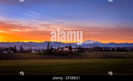 Blauer, orangefarbener und gelber Himmel bei Sonnenaufgang im Fraser Valley von British Columbia, Kanada mit Mount Baker im Staat Washington im Hintergrund Stockfoto