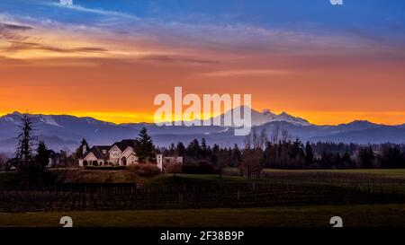 Blauer, orangefarbener und gelber Himmel bei Sonnenaufgang im Fraser Valley von British Columbia, Kanada mit Mount Baker im Staat Washington im Hintergrund Stockfoto