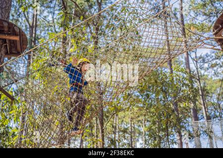 Glückliches Kind im Helm, gesunder Teenager Schuljunge, der an einem Sommertag in einem Kletterabenteuer-Park aktiv ist Stockfoto