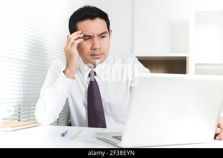 Asiatischer Geschäftsmann immer gestresst (verärgert) bei der Arbeit, indem er seine Hand auf Tempel Stockfoto