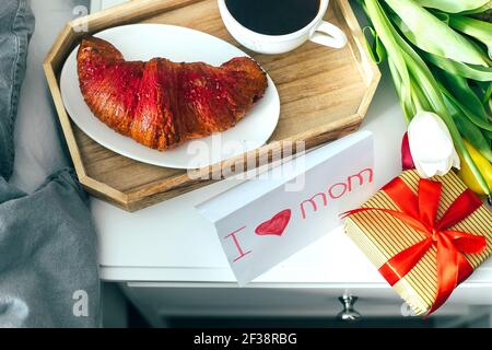 Frühstückstasse, Croissant in Holztablett mit Geschenk und Tulpen serviert. Muttertag, 8. märz, valeentiner Tageskonzept Stockfoto