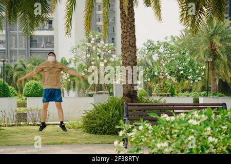 Sportlicher junger asiatischer Mann mit Gesichtsmaske beim Joggen und Laufen im Park. Selektiver Fokus. Stockfoto