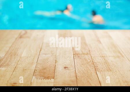 Holztischplatte auf verschwommenem Hintergrund des Swimmingpools mit Wenige Menschen Stockfoto