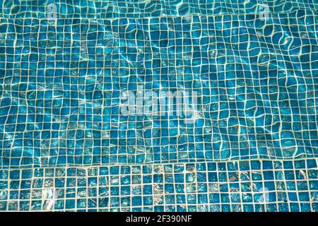 Ein Pool mit blauen Keramikfliesen und Wasserwelligkeit Effekt. Rückbefall von blauem Wasser im Schwimmbad mit Ripple. Nahaufnahme einer türkisfarbenen Mosaikfliesen Stockfoto
