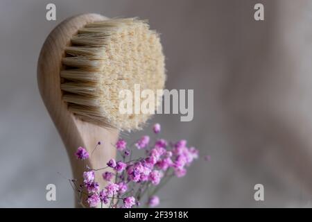 Gesichtsmassagebürste mit natürlichen Borsten auf Leinenhintergrund mit Rinde und rosa Gipsophila-Blüten. Umweltfreundliches Kosmetikkonzept. Stockfoto