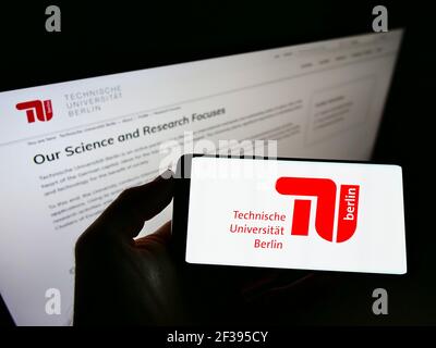 Person, die das Smartphone mit dem Logo der Technischen Universität Berlin auf dem Bildschirm vor der Website hält. Konzentrieren Sie sich auf die Telefonanzeige. Stockfoto