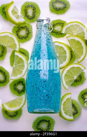 Blaues gekühltes Getränk mit Samen in einer Glasflasche auf tropischem Hintergrund aus Limettenscheiben und Kiwi, Zitrone. Draufsicht. Limonade im Sommer. Weich Stockfoto
