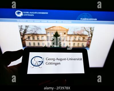 Person, die das Mobiltelefon mit dem Logo der deutschen Bildungseinrichtung Universität Göttingen auf dem Bildschirm vor der Webseite hält. Konzentrieren Sie sich auf die Telefonanzeige. Stockfoto