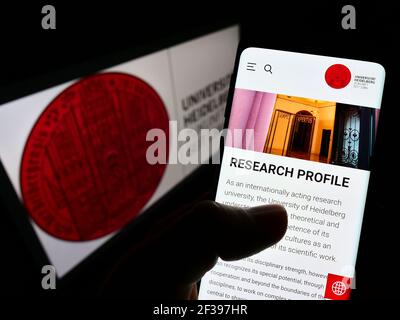Person, die Mobiltelefon mit der Webseite der Deutschen Universität Heidelberg auf dem Bildschirm vor dem Logo hält. Konzentrieren Sie sich auf die Mitte des Telefondisplays. Nicht modifiziertes Foto. Stockfoto