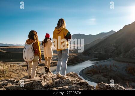 Drei weibliche Touristen oder Wanderer stehen auf Klippe und Blick auf Sonnenuntergang Fluss und Berge Stockfoto