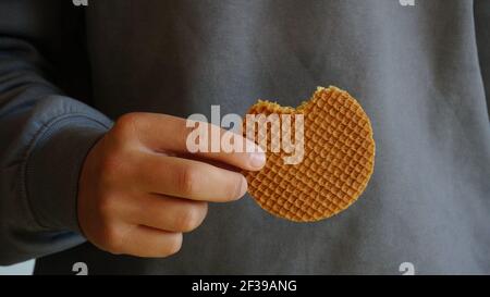 Junger Mann hält holländische Karamell Waffel traditionelle handgemachte Dessert grau sweatshirt im Hintergrund Stockfoto