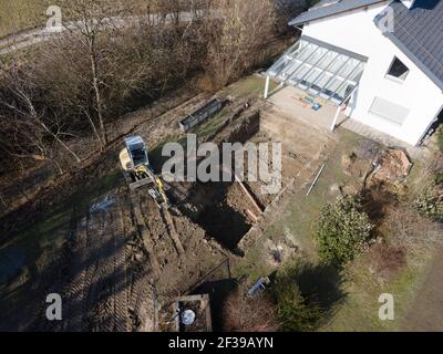 Drohnen Luftaufnahme einer Baustelle eines Pools, kleiner gelber Bagger gräbt Loch für Pool und ist fast fertig in einem schönen Garten in österreich Stockfoto