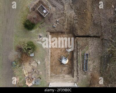 Drohnen Luftaufnahme einer Baustelle eines Pools, kleiner gelber Bagger gräbt Loch für Pool und ist fast fertig in einem schönen Garten in österreich Stockfoto