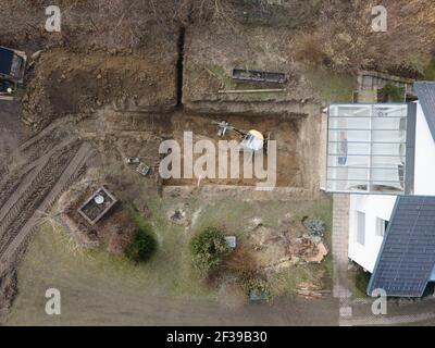 Drohnen Luftaufnahme einer Baustelle eines Pools, kleiner gelber Bagger gräbt Loch für Pool und ist fast fertig in einem schönen Garten in österreich Stockfoto