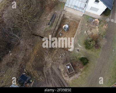 Drohnen Luftaufnahme einer Baustelle eines Pools, kleiner gelber Bagger gräbt Loch für Pool und ist fast fertig in einem schönen Garten in österreich Stockfoto