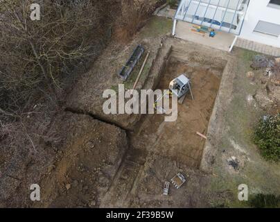 Drohnen Luftaufnahme einer Baustelle eines Pools, kleiner gelber Bagger gräbt Loch für Pool und ist fast fertig in einem schönen Garten in österreich Stockfoto