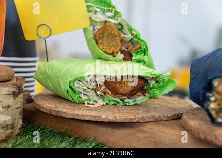 Falafel-Sandwich in flachem grünem Brot gerollt. Veganes Sandwich in Lavaschbrot mit Gemüse und frittiertem Ball oder Patty-förmigen Fritter aus grou Stockfoto