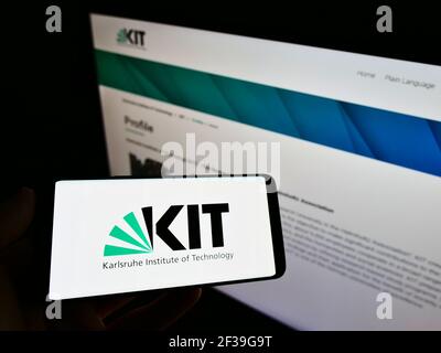 Person, die das Mobiltelefon mit dem Logo des Karlsruher Instituts für Technologie (KIT) auf dem Bildschirm vor der Webseite hält. Konzentrieren Sie sich auf die Anzeige des Mobiltelefons. Stockfoto