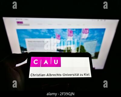 Person, die das Smartphone mit dem Logo der Christian-Albrechts-Universität zu Kiel auf dem Bildschirm vor der Website hält. Konzentrieren Sie sich auf die Telefonanzeige. Stockfoto