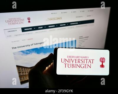 Person mit Mobiltelefon und Logo der deutschen Bildungseinrichtung Universität Tübingen auf dem Bildschirm vor der Webseite. Konzentrieren Sie sich auf die Telefonanzeige. Stockfoto