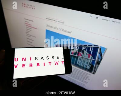 Person, die das Smartphone mit dem Logo der deutschen Bildungseinrichtung Universität Kassel auf dem Bildschirm vor der Website hält. Konzentrieren Sie sich auf die Anzeige des Mobiltelefons. Stockfoto