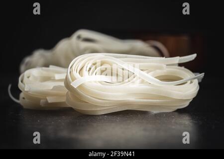 Getrocknete weiße Reisnudeln. Rohe Pasta. Ungekochte Nudeln auf schwarzem Tisch. Stockfoto