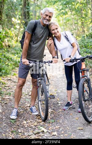 Porträt eines lächelnden reifen Paares mit Fahrrädern, die im Wald stehen Stockfoto