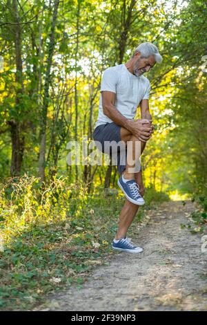 Reifer Mann mit Knieschmerzen, während er im Wald steht Stockfoto