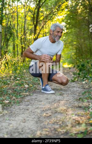 Reifer Mann mit Knieschmerzen beim hocken im Wald Stockfoto