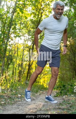 Reifer Mann, der unter Oberschenkelschmerzen leidet, während er im Wald steht Stockfoto