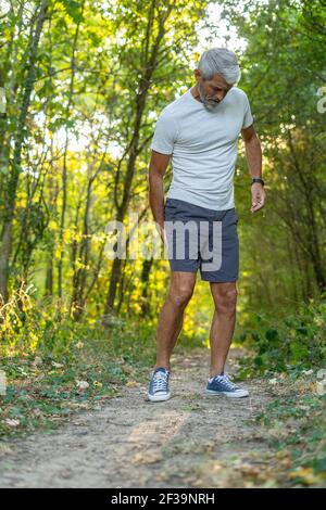 Reifer Mann, der unter Oberschenkelschmerzen leidet, während er im Wald steht Stockfoto