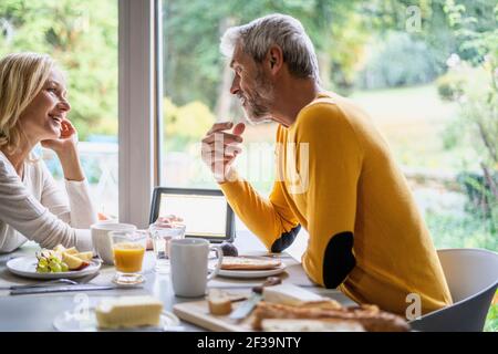 Lächelndes reifes Paar, das sich beim Frühstück unterhielt Stockfoto