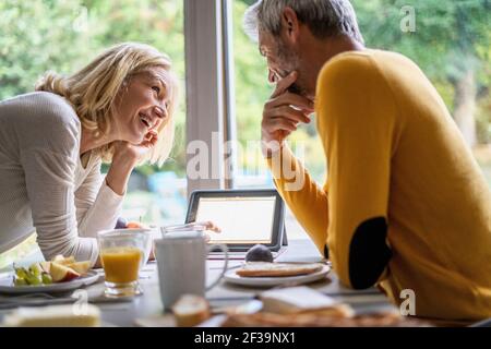 Lächelndes reifes Paar mit digitalem Tablet beim Frühstück Stockfoto