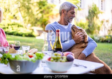 Reifer Mann, der mit Hund spielt, während er am Tisch sitzt Stockfoto