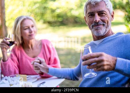 Porträt eines reifen Mannes, der die Hand seiner Frau hält und im Hinterhof Rotwein trinkt Stockfoto