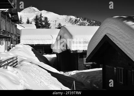 Monochrome Chalets unter tiefem Schnee auf einer schneebedeckten Gasse Mit blauem Himmel in einem Skigebiet Stockfoto