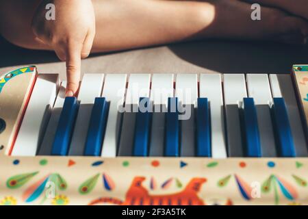 Kaukasisches Kind sitzt auf dem Boden und spielt Klavier Spielzeug mit einem Finger Stockfoto