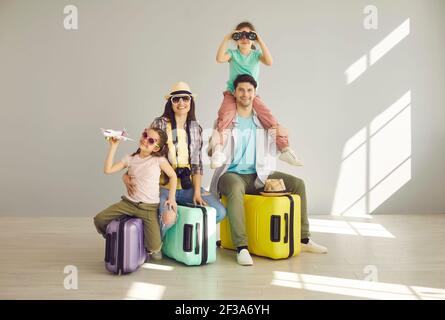Familie in bunten Sommer-Outfits und mit verpackten Koffern warten auf Sommerurlaub. Stockfoto
