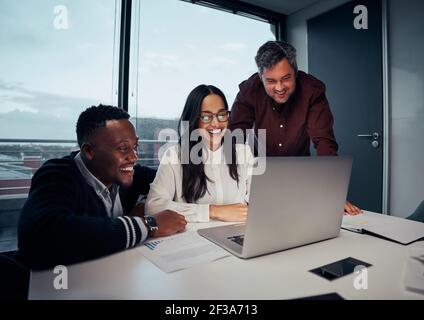 Glückliche, multiethnische Gruppe von Geschäftsleuten, die sich über Laptops unterhalten Neues Projekt im Büro Stockfoto
